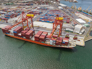 Aerial view of a large cargo ship getting loaded with containers by cranes at a port