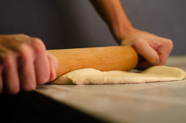 Man's hands with a wooden rolling pin kneading pizza dough