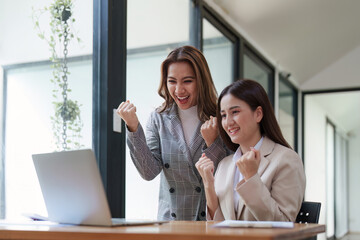 Asian business team happy to be successful partnership teamwork celebrating achievement and success concept. Beautiful business team celebrate with laptop