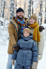 Portrait of happy family with child embracing and smiling at camera during their walk in winter