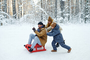 Family of three having fun during winter vacation, they sledding in the forest