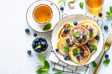 Healthy breakfast. Pancakes with fresh blueberries and honey at white table, served with mint leaves. Top view with copy space.