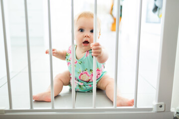 Crawling baby in kitchen holding onto bars of safety baby gate