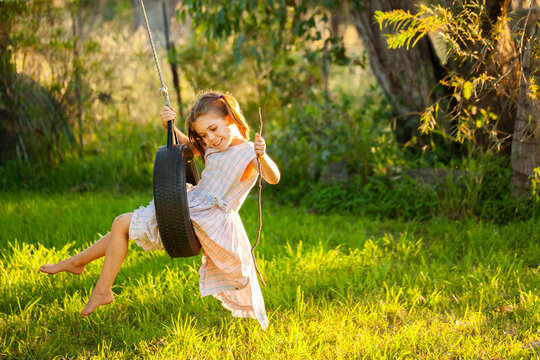 Young country kid in dress swinging on tyre swing in tree outside