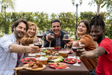 Happy trendy family cheering with red wine at barbecue lunch outdoor, different age of people having fun at sunday meal, food, taste and unity concept, focus on mature man sitting at the head