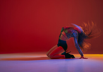 Passion and sensuality. Portrait of young girl dancing heels dance over red background in neon with...