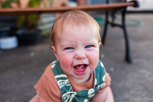 Baby laughing and pulling face outside playing in overalls