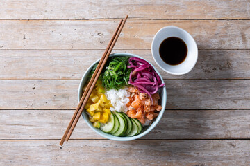 Poke bowl with rice, salmon,cucumber,mango,onion,wakame salad, poppy seeds ands sunflowers seeds on wooden background. Top view
