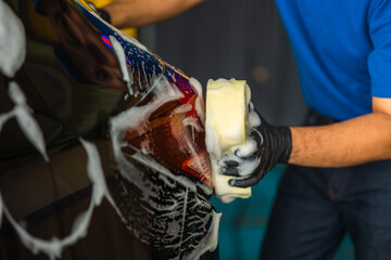 Fototapeta premium Man worker washing car service with foam and sponge. Car wash cleaning wipe station. Employees clean a vehicle professionally.