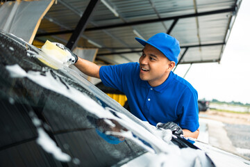 Man worker washing car service with foam and sponge. Car wash cleaning wipe station. Employees clean a vehicle professionally.