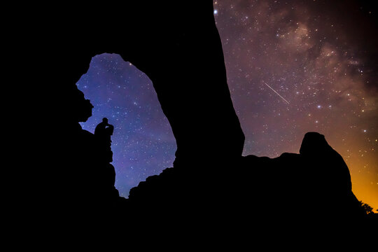 A silhouetted figure sits under an arch at night.