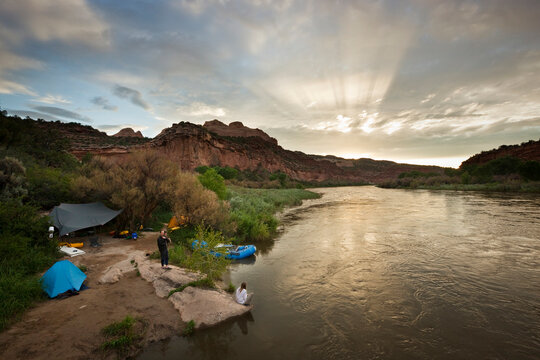A group of people camp after rafting on the Colorado River at sunset.
