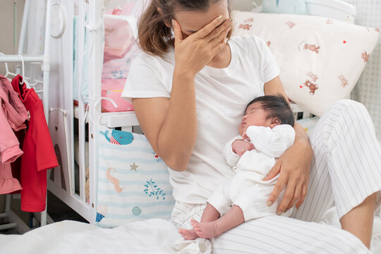 tired mother suffering from experiencing postnatal depression sitting on bed near children's cot. mother sleeping embracing to her asleep baby daughter sitting at home. single mom motherhood stressful