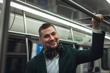 man young male caucasian passenger one person positively cheerful listens to music in headphones, smiles and go by subway transport in the morning. concept subscription to music.