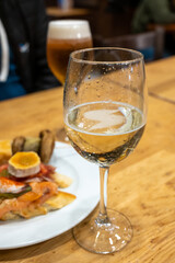 Board with typical snacks of Basque Country, pinchos or pinxtos, skewers or small piece of bread with toppings, served with glass of txakoli wine in bar in San-Sebastian or Bilbao, Spain