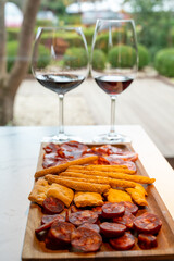 Wooden plate with sliced Spanish tapas, choriso sausage, lomo iberico en bread sticks served with glass of red wine