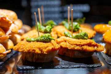 Typical snack of Basque Country, pinchos or pinxtos skewers with small pieces of bread, sea food, eggs, cheese, jamon served in bar in San-Sebastian or Bilbao, Spain