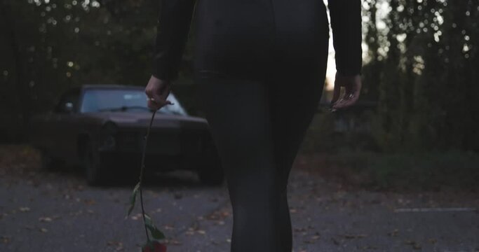 frau l&auml;uft mit rose in der hand zu einem auto. dresscode leder und latex. in slow motion