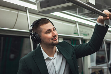 man young male caucasian passenger one person positively cheerful listens to music in headphones, smiles and go by subway transport in the morning. concept subscription to music.
