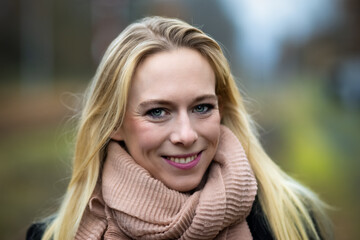 Naklejka premium Woman young blond head portrait, warmly dressed with a scarf smiles at the camera..