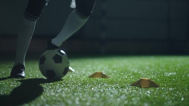dribbling ball in football hall, closeup of legs of soccer player, running over artificial grass