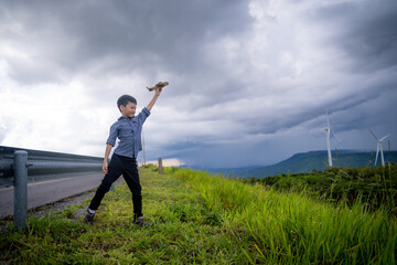 Fototapeta na wymiar Happy Asian boy playing toy plane with wind turbine in the background.