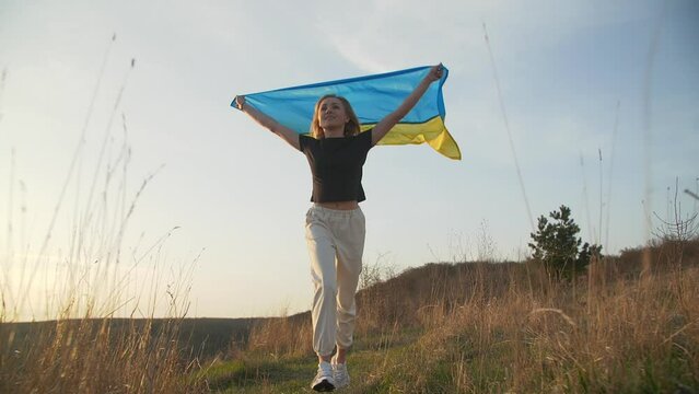 A young girl is holding Ukrainian flag over her head and running on sunset nature background. She is proud to be Ukrainian. Slow mo. High quality FullHD footage