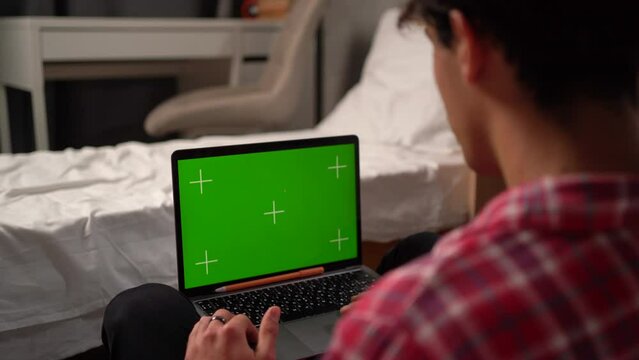 Close-up On The Hands Of A Guy Student In A College Dorm Working On Laptop With A Green Screen Mockup. Chatting With Friends Over The Internet