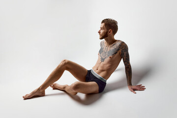 Fototapeta na wymiar Studio shot of young blonde man with beard and moustache posing shirtless. Perfect muscular body shape. Tattoo body art. Concept of fashion, style, body aesthetics, beauty, men's health