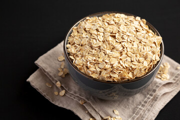 Wholegrain Oat Flakes in a Bowl on a black background, side view. Copy space.