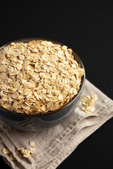 Wholegrain Oat Flakes in a Bowl on a black background, side view.