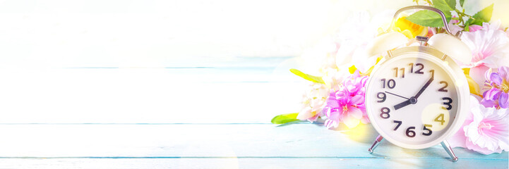 Spring Time Change concept. Summer back concept. Vintage alarm Clock with fresh, beautiful spring flower on sun lighted background banner background copy space