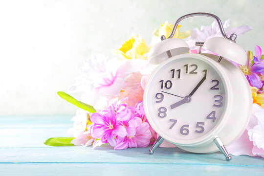 Spring Time Change concept. Summer back concept. Vintage alarm Clock with fresh, beautiful spring flower on sun lighted background banner background copy space