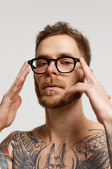 Close up portrait of charming bearded man in eyewear looking at camera confidently over grey background. Concept of emotions, mental health, fashion