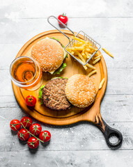 Burgers with beer, tomatoes and French fries on the cutting Board.