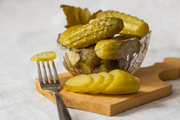Crispy pickles in a transparent glass bowl on the table with a linen tablecloth. Whole green small cucumbers with dill and garlic. Delicious canned vegetables. We close cucumbers for the winter.