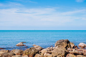 Rock in the smooth sea or ocean with clear cloud and blue bright sky background at the sandy beach on summer time