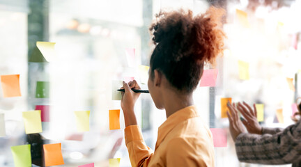 Fototapeta Young businesswoman creative team using post it notes in glass wall to writing strategy business plan to development grow to success. obraz