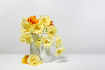 Yellow and orange hybrid tulips in a white vase on a white table.