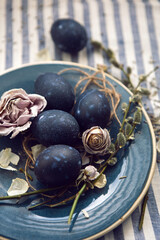 blue Easter eggs lie on a plate with a willow on a striped fabric background