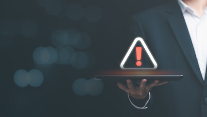 Businessman holding a tablet and showing a warning icon, exclamation mark,alarm,computer virus detected,danger warning concept or information error that should be urgently fixed and repaired - obrazy, fototapety, plakaty