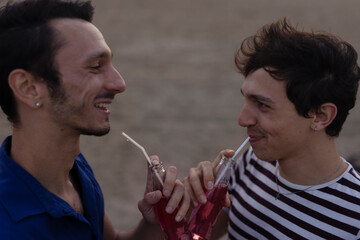 Happy young couple enjoy at the beach. Men drinking juice. LGBT community