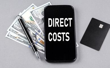 Credit card and text DIRECT COSTS on smartphone with dollars and pen. Business