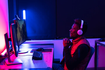 Young African man playing video game on computer. Streamer guy sitting at home and plays another match.