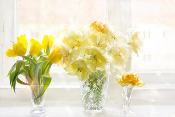 Yellow tulips in three vases on a white windowsill illuminated by sun.