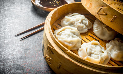 Hot aromatic manta dumplings in bamboo steamer with soy sauce.