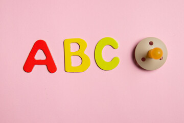 The composition of ABC multicolored letters red, yellow, green and the baby pacifier on the pink...
