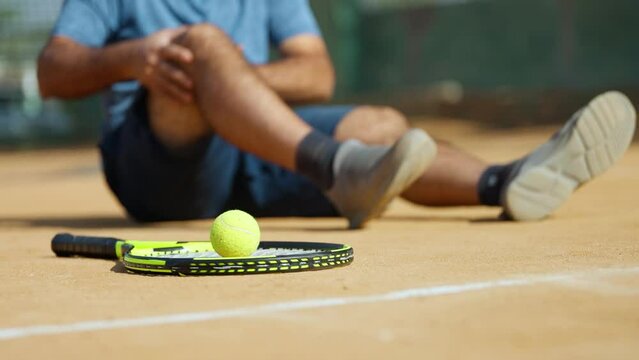 Close up shot of fallen injured senior man suffering from knee pain while playing tennis at court - concept of emergency, painful and inflammation
