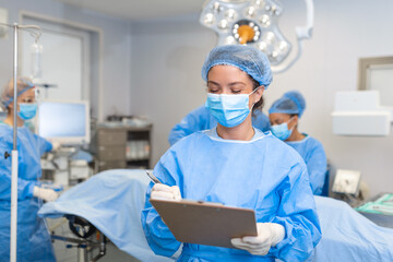 Surgeon writing on clipboard in operation room, anaesthesiologist writing the updates