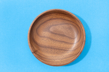 Empty round wooden plate or bowl isolated on blue background. Walnut wood. Top view